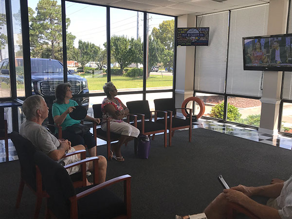 a group of people sitting in a waiting room all looking at an ad on a dynamic digital billboard screen