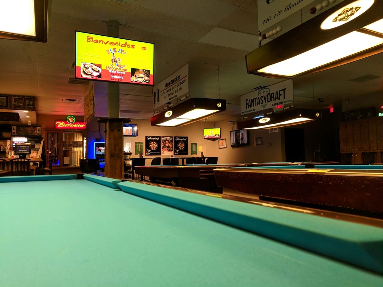 Blue pool tables in a dimly lit billiard hall, wiht a bright tv displaying dynamic digital Indoor billboard ads